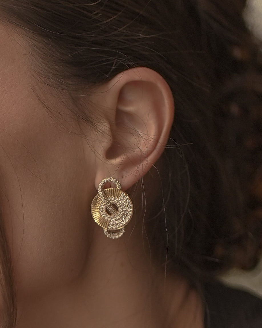 Woman wearing Inara by Sneha gold earrings and Inara bracelet with a flower blurred background