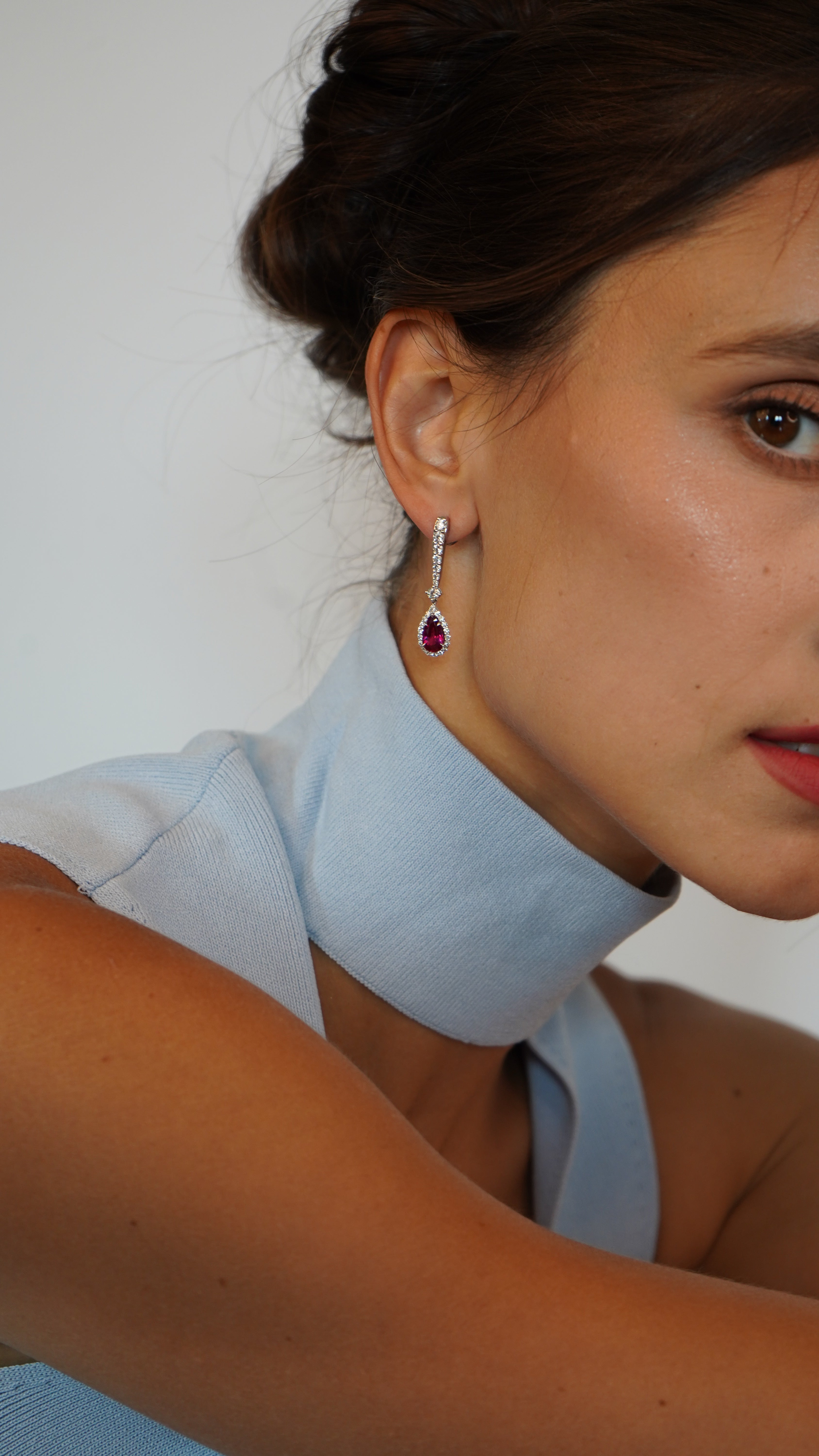 Woman wearing gold earrings with a ruby gemstone.
